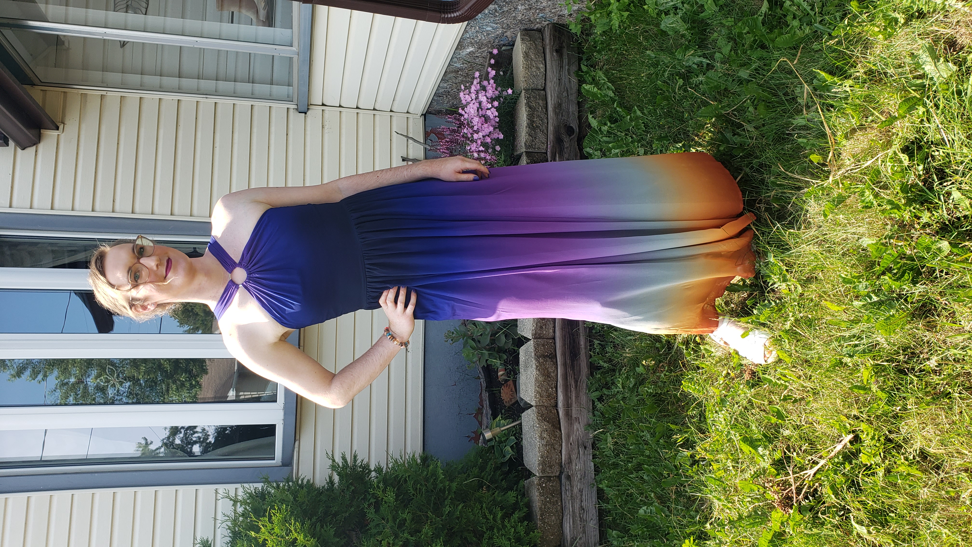 I'm wearing a halterneck ombre dress from navy to purple to grey to orange, standing outside in front of my house and a garden.